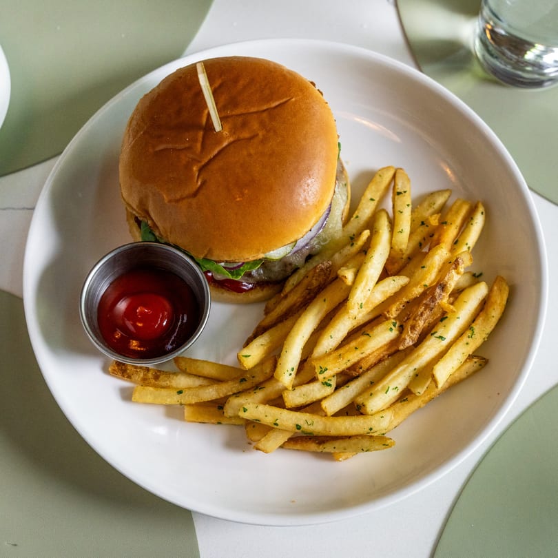 A burger with fries and a side of ketchup on a white plate.