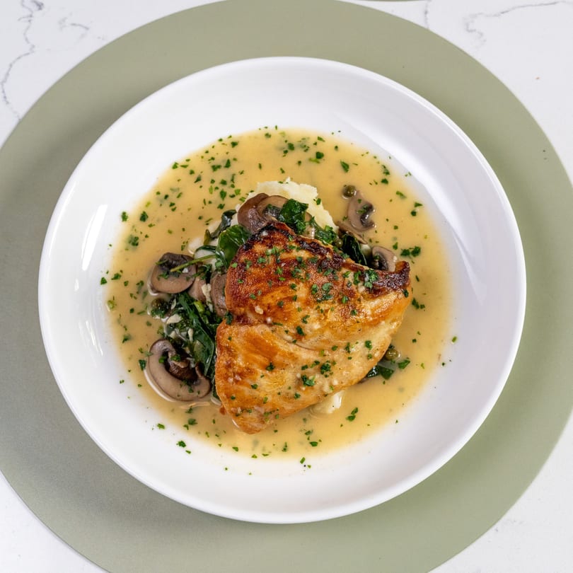 Pan-seared fish with mashed potatoes, spinach, mushrooms, and a creamy sauce on a white plate.