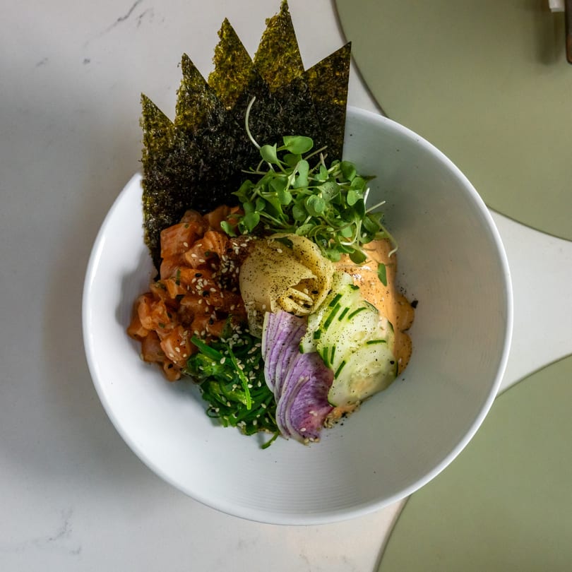 A vibrant poke bowl with salmon, seaweed, microgreens, pickled ginger, cucumber, and red onion.
