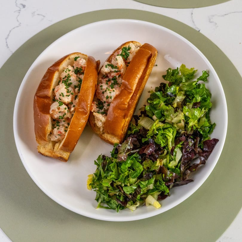 Two lobster rolls with chives and a side salad on a white plate.
