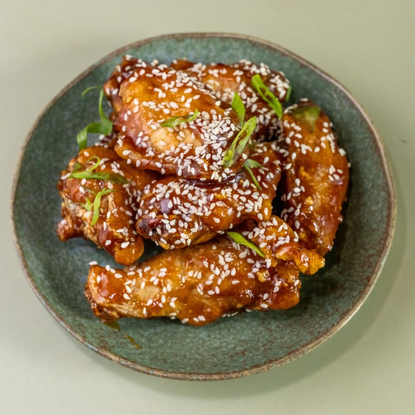 Sweet and sticky chicken wings, garnished with sesame seeds and green onions, on a green plate.